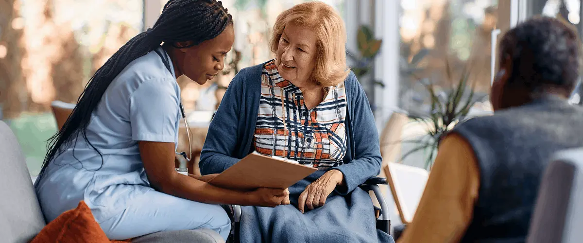 Care home manager reviewing resident records with an elderly woman in a wheelchair, reducing administrative burden through face-to-face care documentation