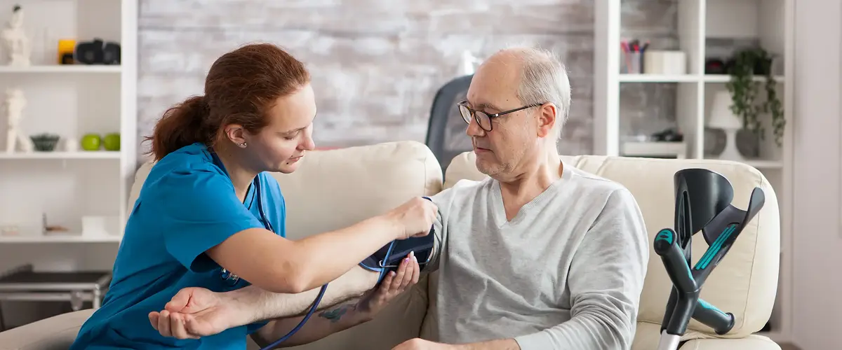Nurse providing person-centred care by checking blood pressure for an elderly male resident in a care home setting